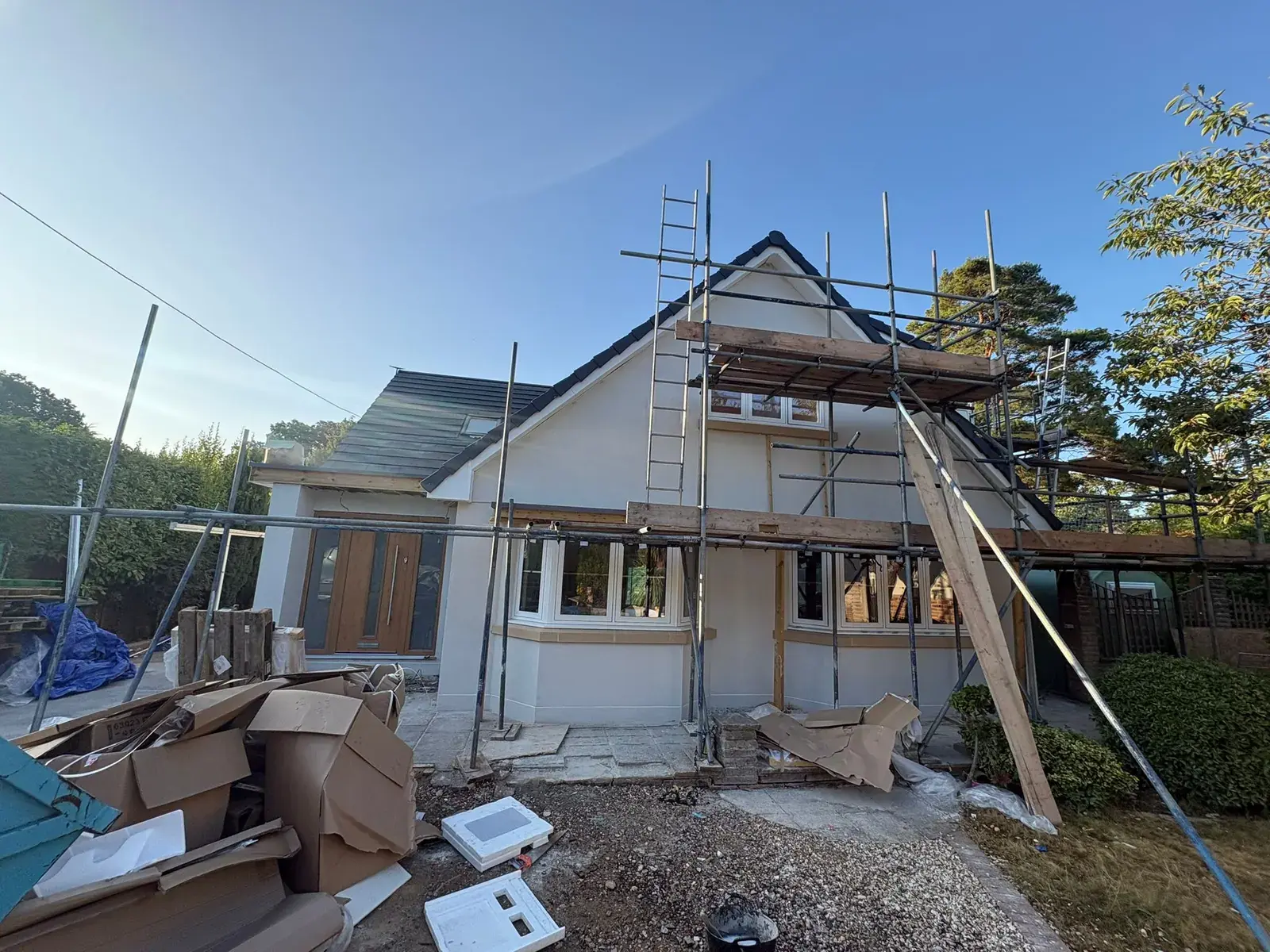 Chalet bungalow on scaffold with the render base coat on, flattened cardboard and materials on the drive