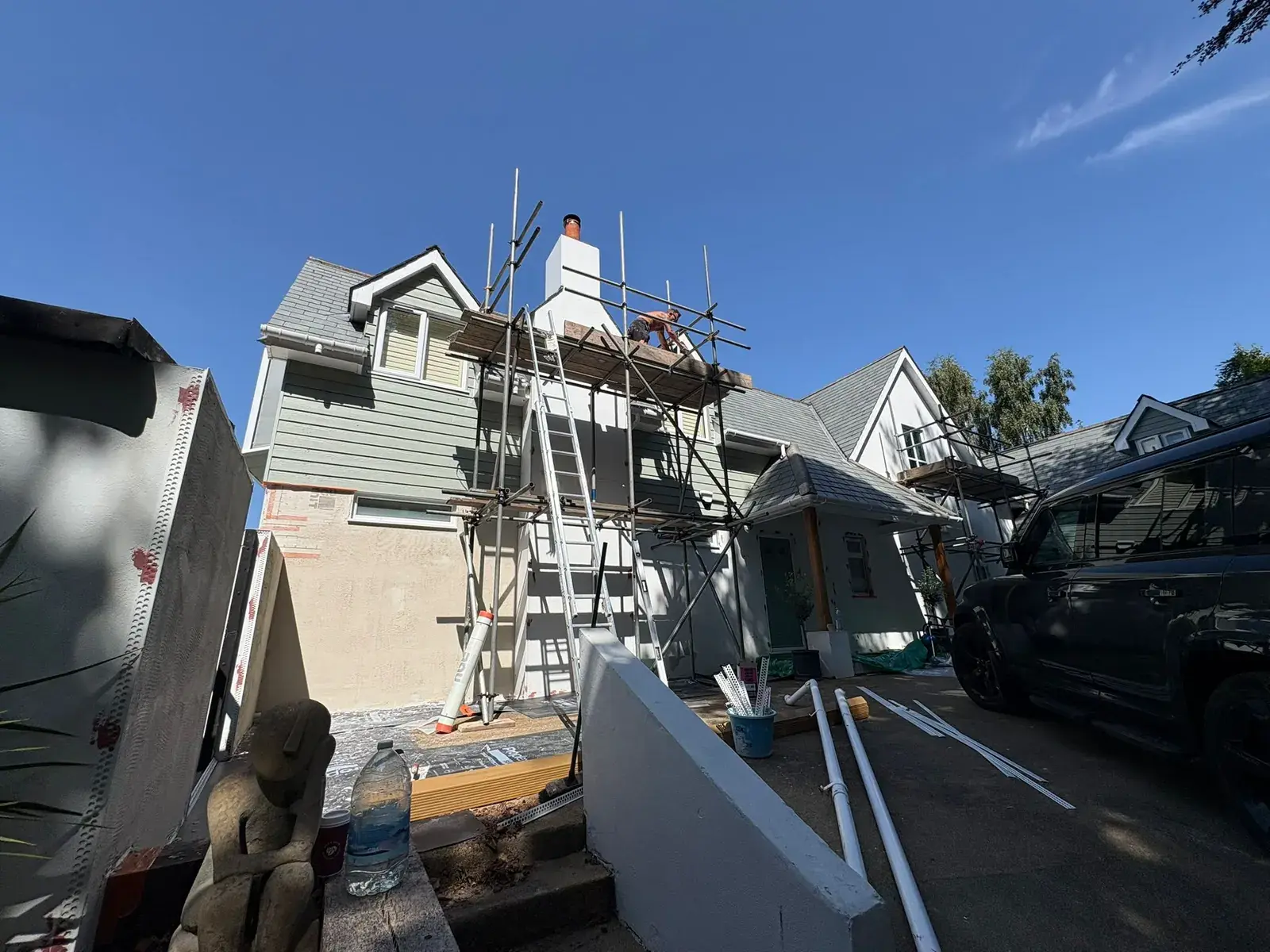 Chalet-style house on scaffold with beads and mesh on the side wall and a plasterer at the chimney