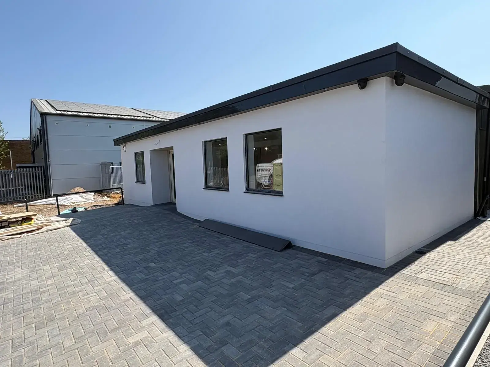 Flat-roof new build finished in white render with dark fascia, block-paved forecourt in front