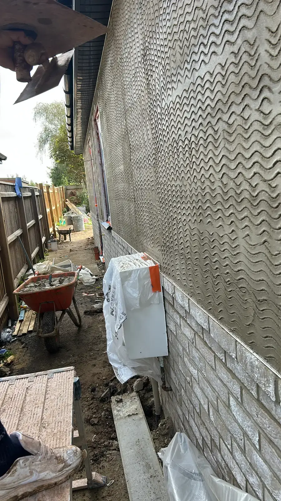 Render scratch coat applied with the wavy comb pattern, wheelbarrow in shot
