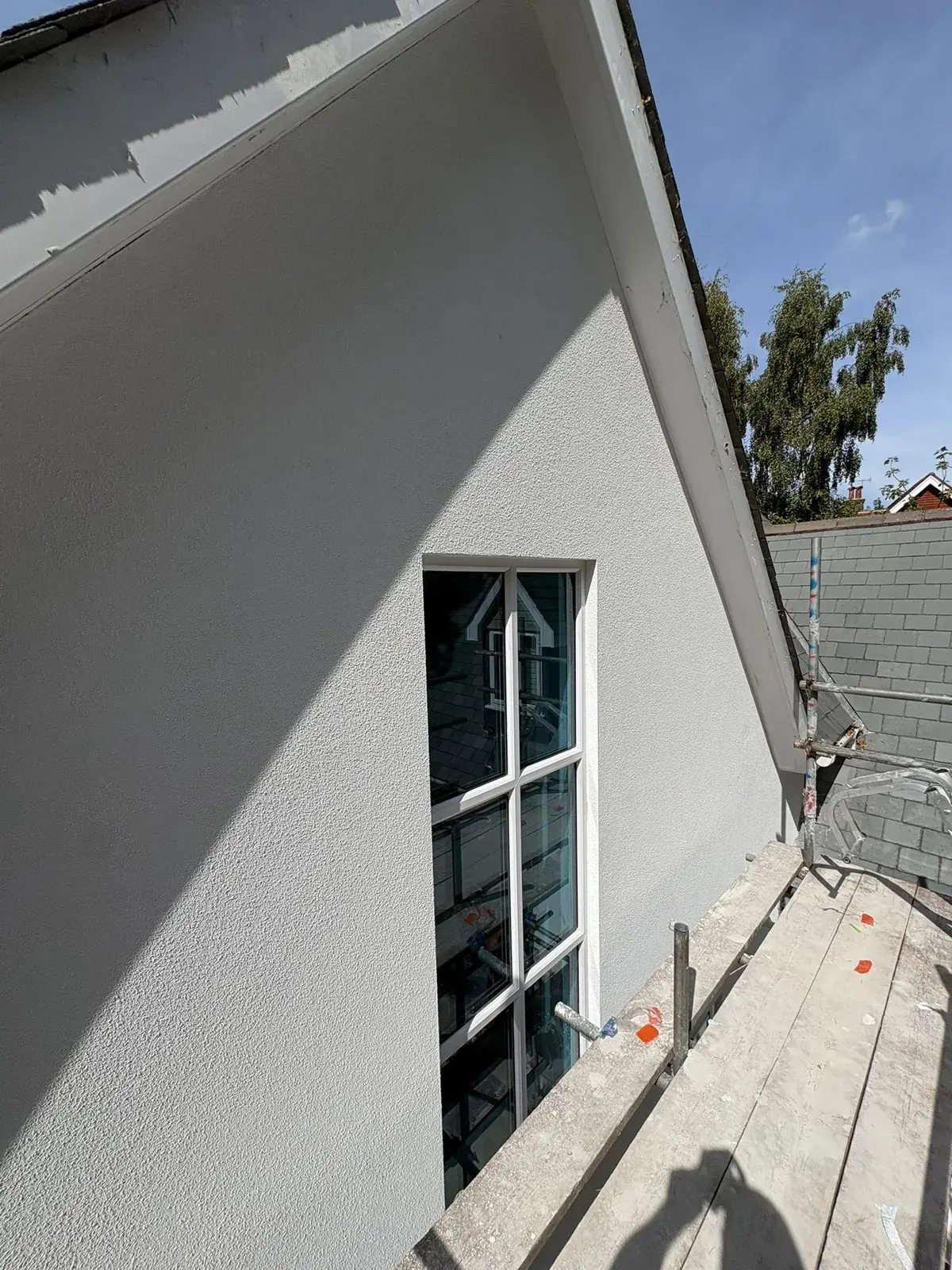 Finished thin-coat render on a gable end with a tall white-framed window, slate roof of the neighbouring house alongside