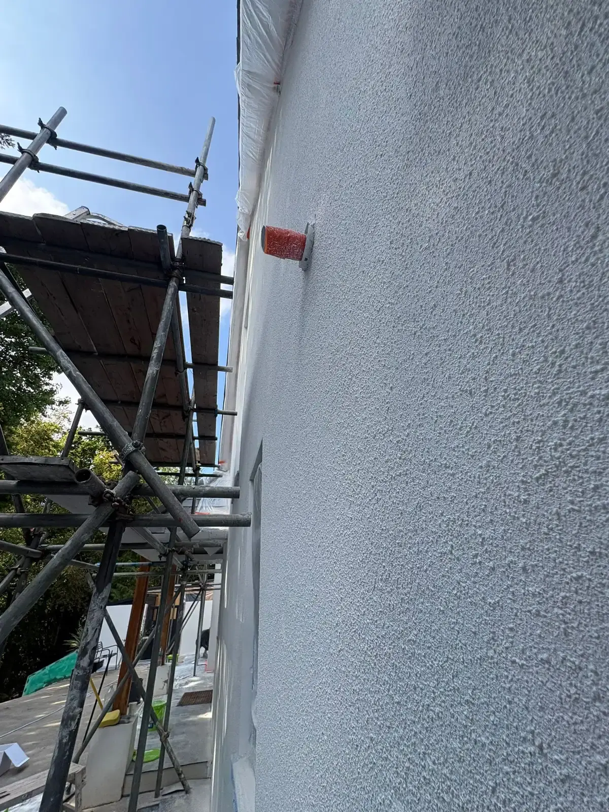 Close-up of a finished light-grey textured render with a vent pipe, scaffold boards alongside